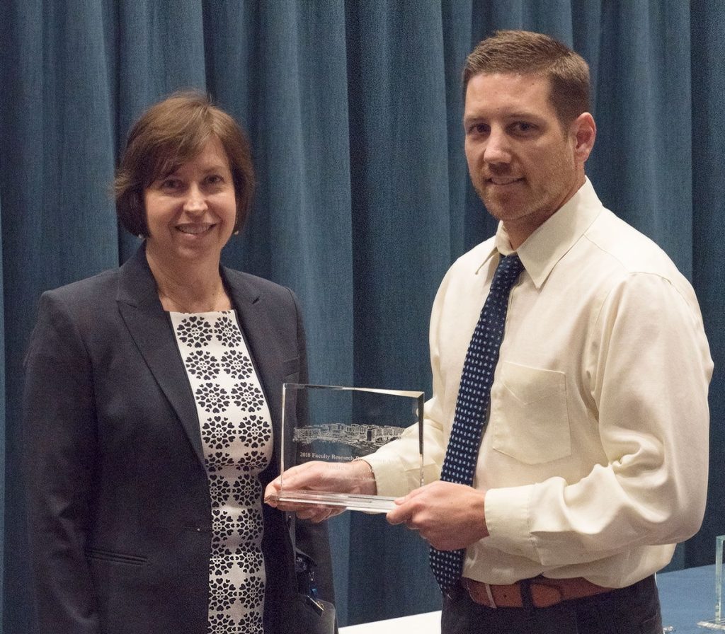 Dr. Andrew Foy is pictured standing with Dr. Leslie Parent after Foy received one of two 2018 Outstanding Research Publication Awards, which he is holding.