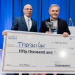 Neil Sharkey, PhD, Vice President for Research, Penn State, left, presents Charles Palmer, MD, and his startup company, ThoraciCair, $50,000 for finishing in second place at the Tech Tournament at the Penn State Venture & IP Conference held in April 2018. The two men are pictured standing next to each other on a stage, both holding a side of a large check made out to ThoraciCair. Palmer is also holding a trophy.