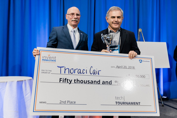 Neil Sharkey, PhD, Vice President for Research, Penn State, left, presents Charles Palmer, MD, and his startup company, ThoraciCair, $50,000 for finishing in second place at the Tech Tournament at the Penn State Venture & IP Conference held in April 2018. The two men are pictured standing next to each other on a stage, both holding a side of a large check made out to ThoraciCair. Palmer is also holding a trophy.