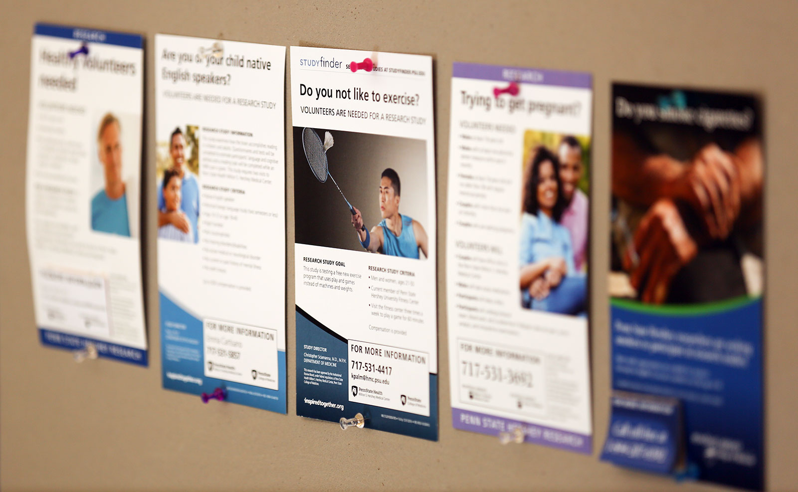 Posters depicting Penn State College of Medicine clinical trials that are seeking volunteers are displayed on a bulletin board.
