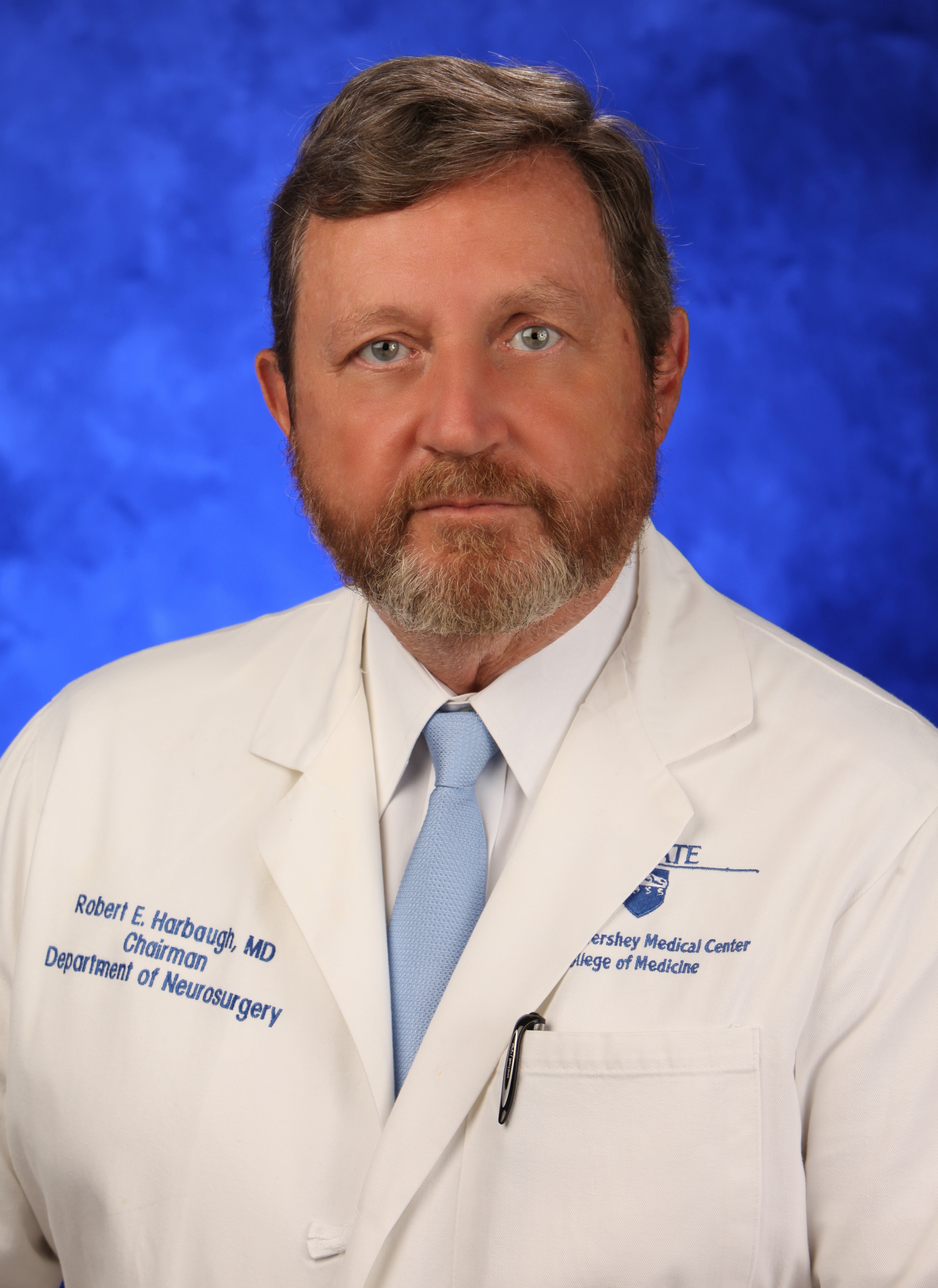 Dr. Robert Harbaugh, chair of the Department of Neurosurgery at Hershey Medical Center and Penn State College of Medicine, is pictured in a head-and-shoulders professional portrait, wearing a medical coat with the medical center and college of medicine’s logos on it.
