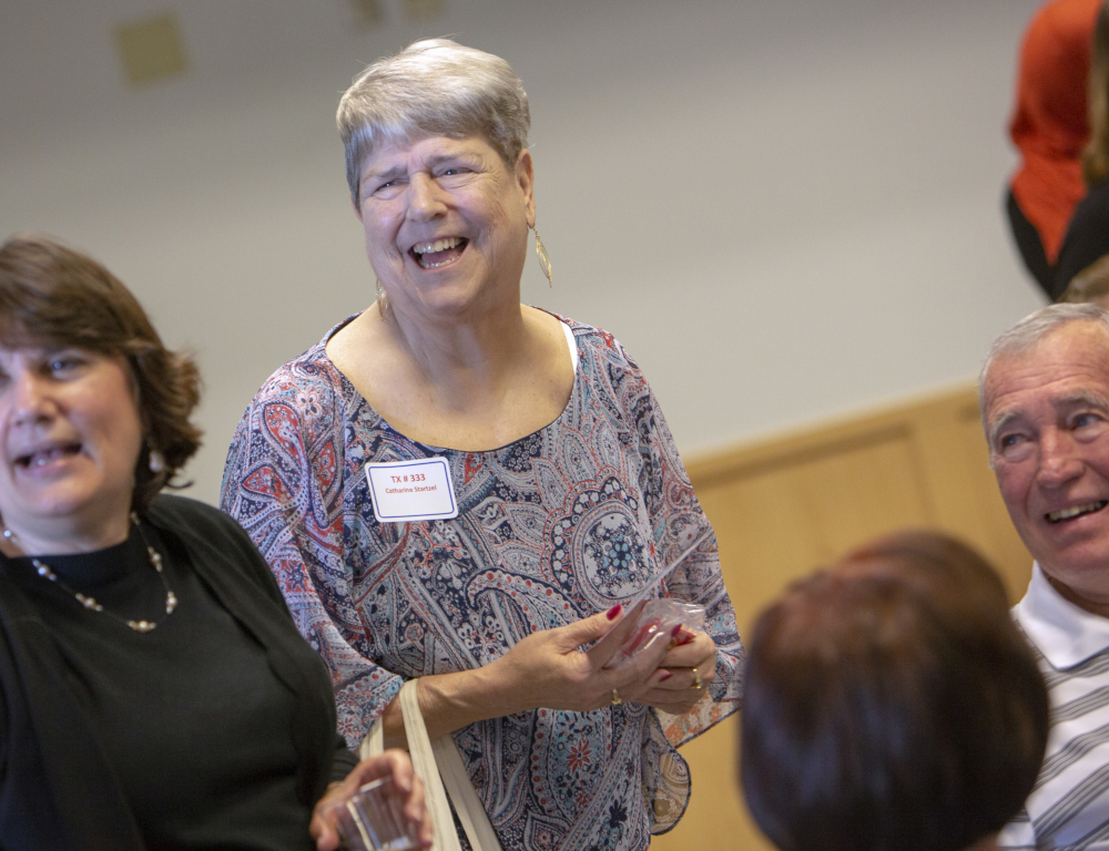 Four people “ two standing, two seated “ are talking to each other. A woman in the middle is laughing.