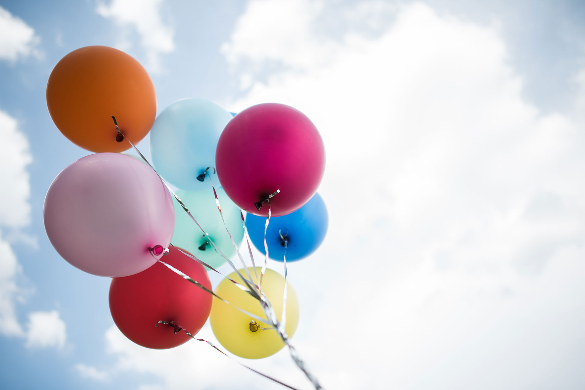 A set of eight balloons in different colors are seen against the background of a cloudy sky.