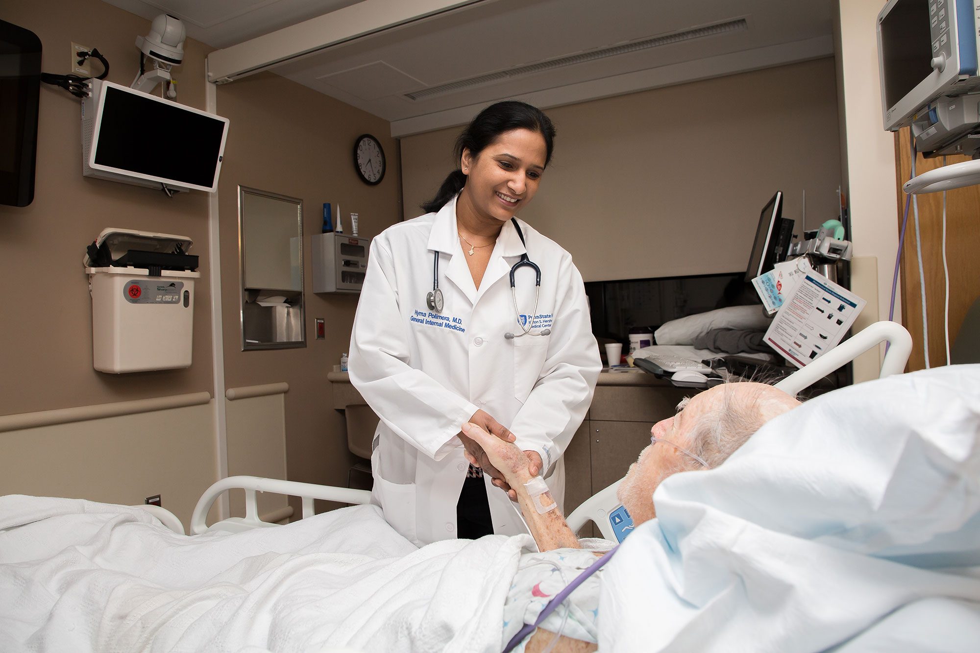 A photo shows Dr. Hyma Polimera at the bedside of a patient at Penn State Health Milton S. Hershey Medical Center.