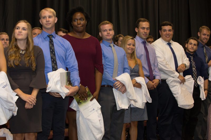 Several medical students stand in a row, holding in front of them their white medical coats.