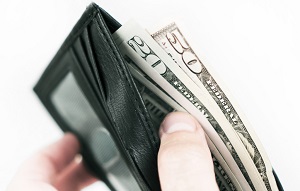 A close up photo of a hand holding a wallet. There is a $50 bill and a $20 bill coming out of the wallet.