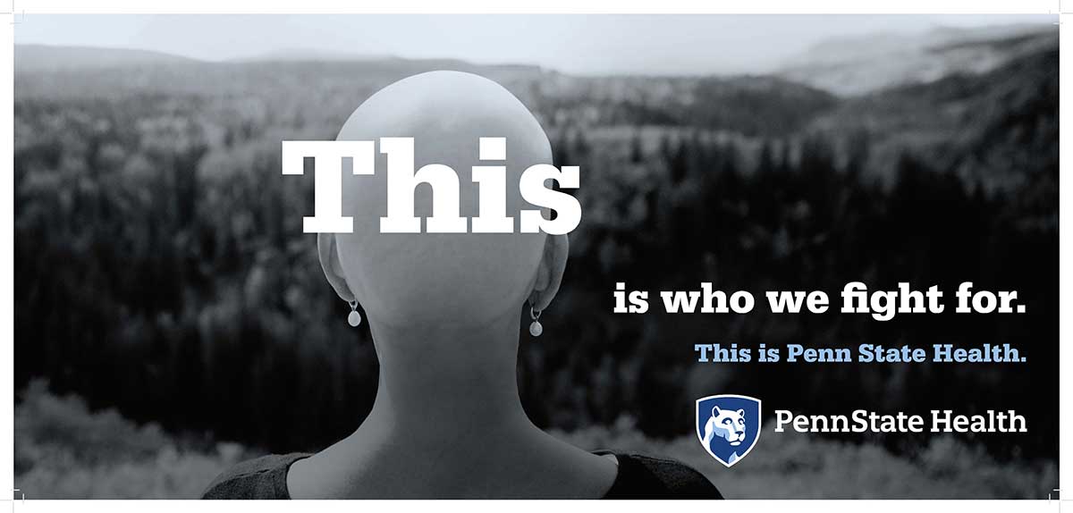 Photo focuses on woman with her back to the camera. She is bald. The photo is taken from behind her looking at the same view she is or mountain views with trees. The text reads, “This is who we fight for. This is Penn State Health.” The logo appears in the lower right corner.