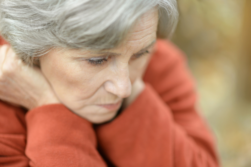 A close up photo of a woman looking down. She has her head resting on both hands on either side of her fact. The background is blurry.