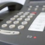 Close up photo of an office desk phone. Photo focuses on the voice mail icon and button at the base of the phone. Photo blurs out toward the top of the phone.
