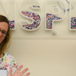 A group of nurses are seen in the Survivorship Clinic at Penn State Children's Hospital. They are making silly faces and gesturing to a large depiction of the word INSPIRE on the wall behind them.