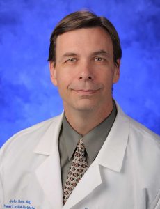 Dr. John Boehmer of Penn State Health Milton S. Hershey Medical Center/Penn State College of Medicine is pictured in a head-and-shoulders professional portrait wearing a white lab coat with the Penn State Heart and Vascular Institute logo on it. He is wearing a shirt and tie.