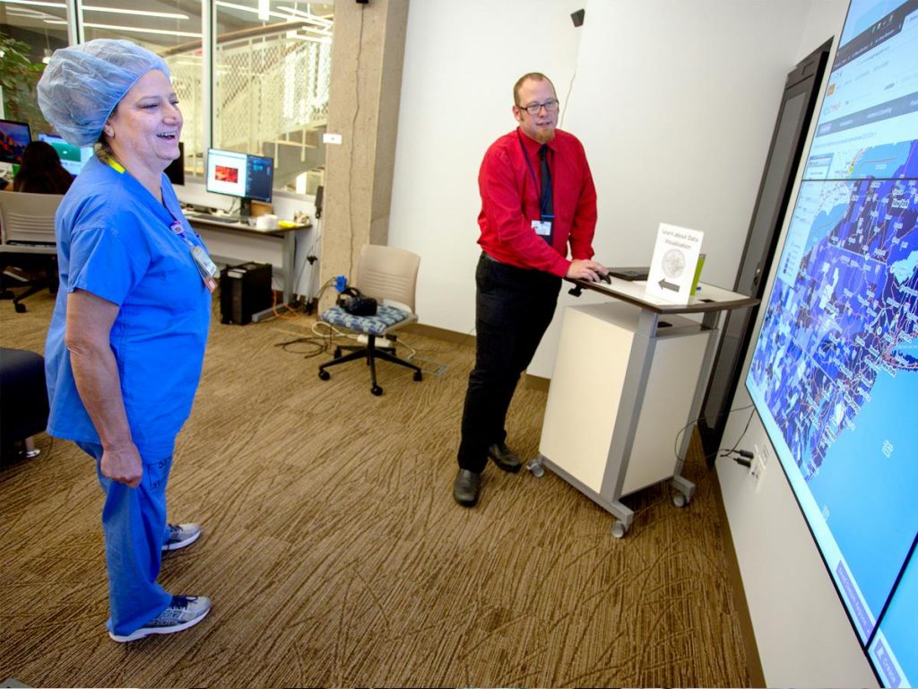 Dale Acela, a registered nurse at Penn State Health Milton S. Hershey Medical Center, gets a lesson in data visualization from Ben Hoover during the Day of Making event at Harrell Health Sciences Library in August 2018. The two are pictured standing in a large room, looking at a big projection screen.