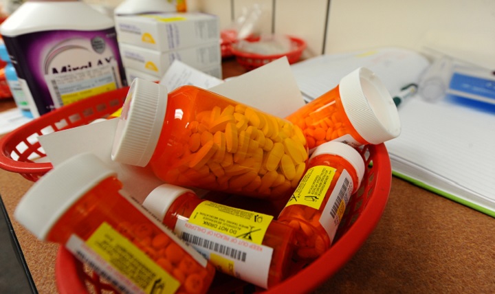 Bottles of prescription pills sit in a basket on a counter. Behind them are other medicine and a book.