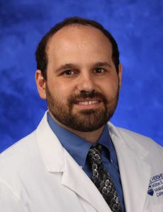 Dr. Michael Freeman of Penn State Health Milton S. Hershey Medical Center/Penn State College of Medicine is pictured in a head-and-shoulders professional portrait wearing a white lab coat with the Penn State Health Milton S. Hershey Medical Center/Penn State College of Medicine logos on it. He has a beard and is wearing a shirt and tie.