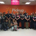 A group of people in Wal-Mart vests pose for a photo with a woman and her young daughter.