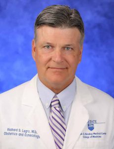 Dr. Richard Legro is seen in a head and shoulders professional wearing a white lab coat with his name, Obstetrics and Gynecology, and the Penn State Health Milton S. Hershey Medical Center logo on it. He is wearing a shirt and striped tie.