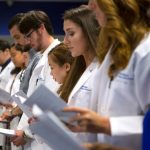 Participants on stage recite the Graduate Student Oath during the Penn State College of Medicine Graduate Oath Ceremony in August 2018. A line of students is pictured holding a paper with the oath printed on it. The students are looking down and reading from the paper.