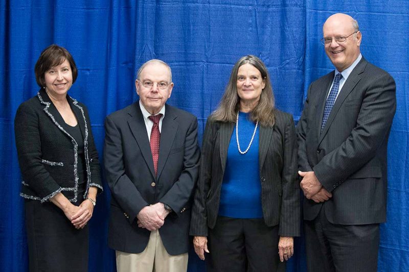 From left, Dr. Leslie Parent smiles with Innovator of the Year Award winners Dr. Joseph Sassani and Patricia McLaughlin and Dr. Craig Hillemeier. They are each wearing business suits and standing in a row smiling. Behind them is a curtain.