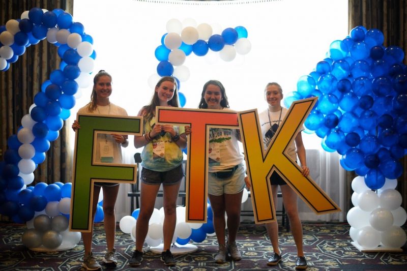 Four teenage girls hold oversized letters that spell out