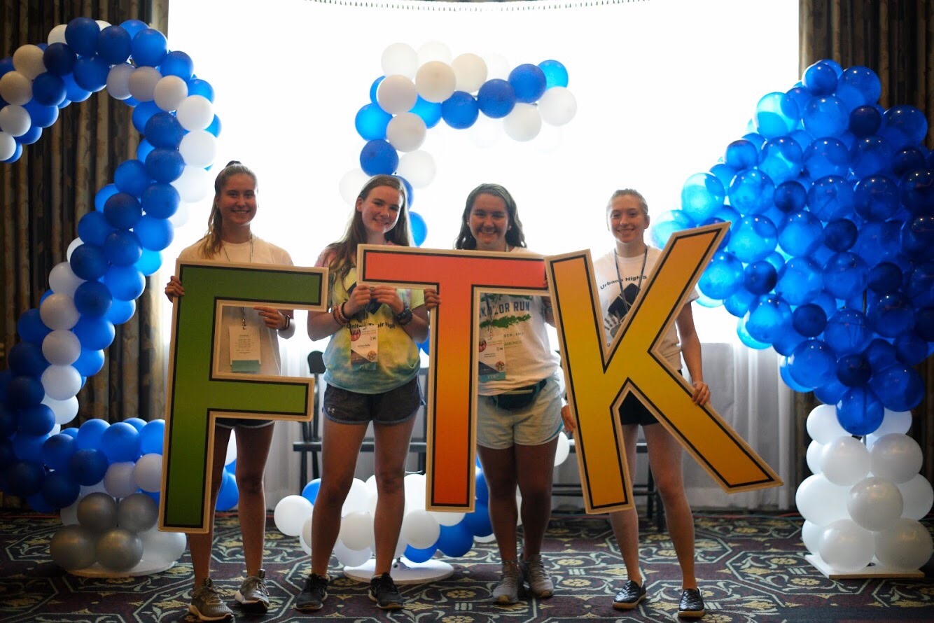 Four teenage girls hold oversized letters that spell out 