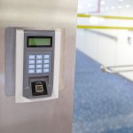 A security entrance electronic door lock with a keypad is mounted on a wall. To the right is a glass door leading to an office.