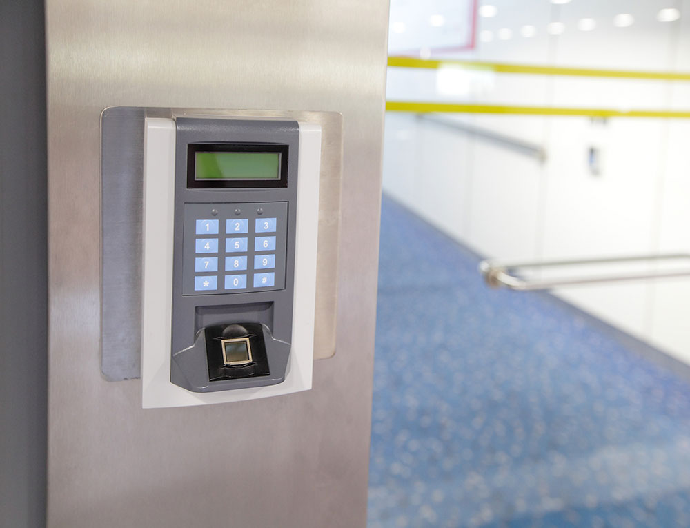 A security entrance electronic door lock with a keypad is mounted on a wall. To the right is a glass door leading to an office.