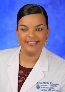 Dr. Sarah Ramirez is seen in a head-and-shoulders professional portrait. She is wearing a white lab coat, a maroon top and gold, dangle earrings.