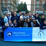 A group photo shows faculty, staff, students and family members holding a banner that says Penn State College of Medicine.