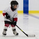 A young child in hockey gear holds a hockey stick and skates on the ice.