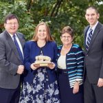 Kristin Lambert is seen standing with her family outdoors. She is holding a small statue of the Penn State Nittany Lion.