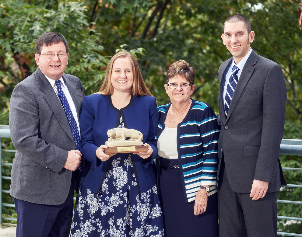 Kristin Lambert is seen standing with her family outdoors. She is holding a small statue of the Penn State Nittany Lion.