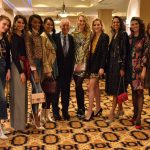 Jeanne and Ed Arnold smile with 10 models at the 2018 Neiman Marcus Runway Show. The models wear a variety of fashions and stand in a row on an ornate carpet.