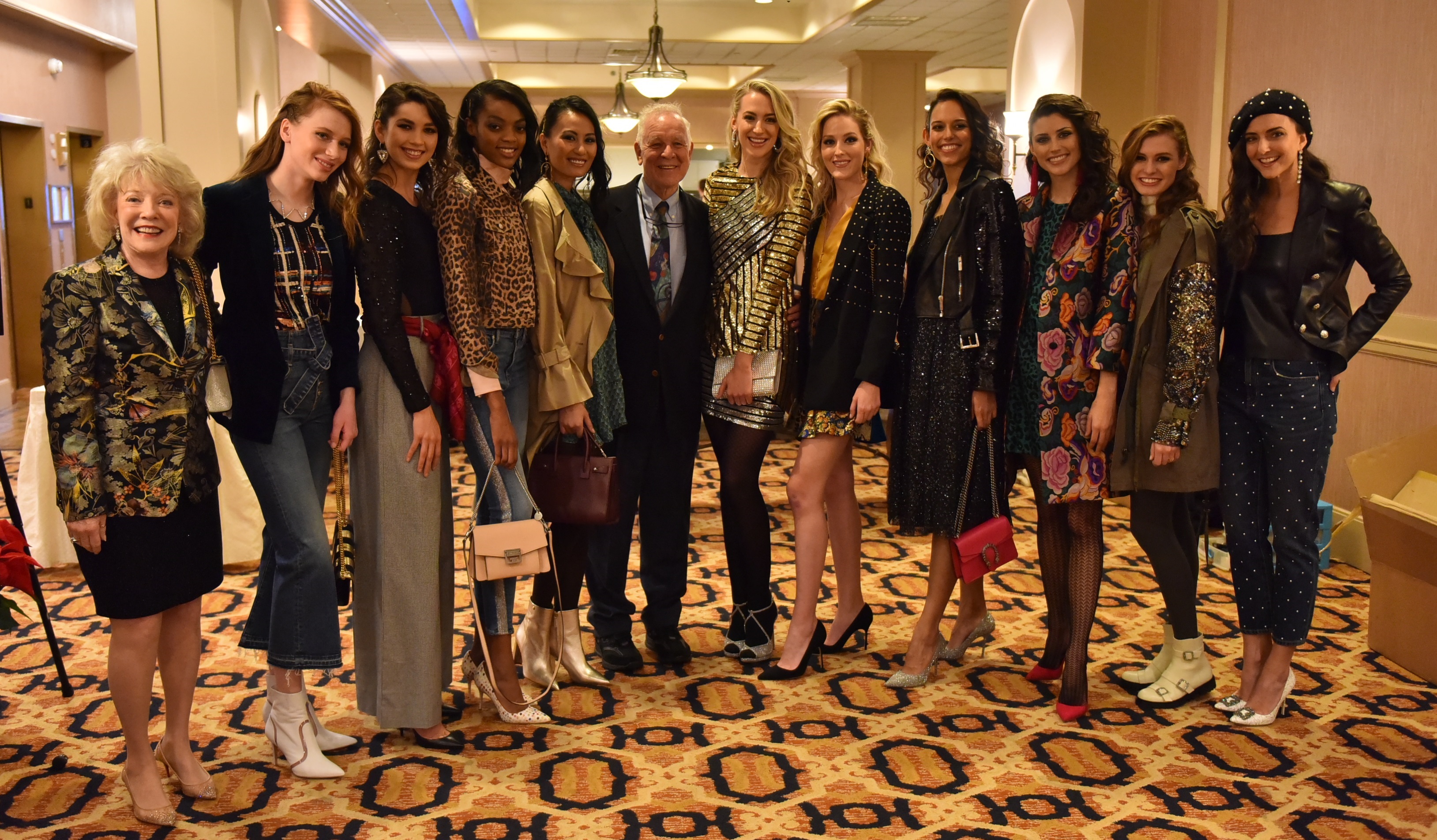 Jeanne and Ed Arnold smile with 10 models at the 2018 Neiman Marcus Runway Show. The models wear a variety of fashions and stand in a row on an ornate carpet.
