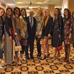 Jeanne and Ed Arnold smile with 10 models at the 2018 Neiman Marcus Runway Show. The models wear a variety of fashions and stand in a row on an ornate carpet.