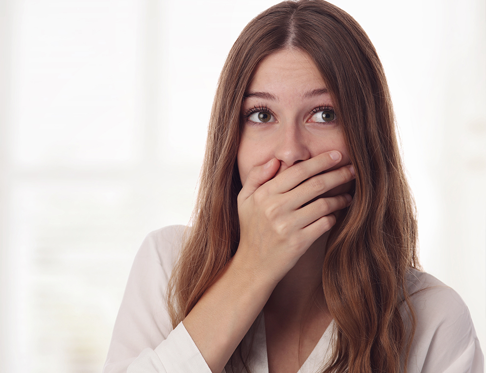 A woman holds her right hand up to cover her mouth, as her eyes look slightly upward and to the side.