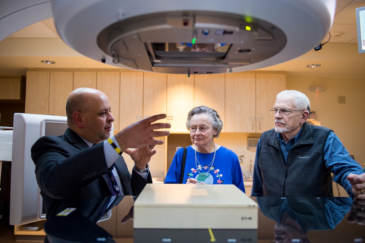 Three people talk next to a. large medical machine