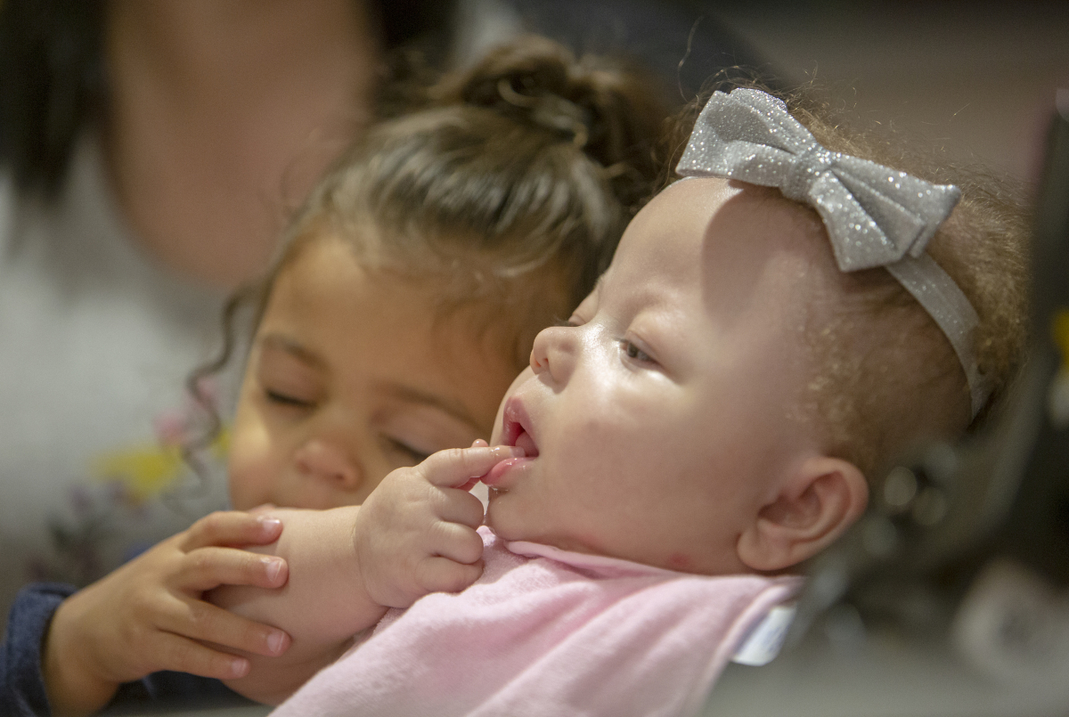 Ramiah Martin sits reclined in a stroller; her sister sits beside her, placing her hand on Ramiah's arm.