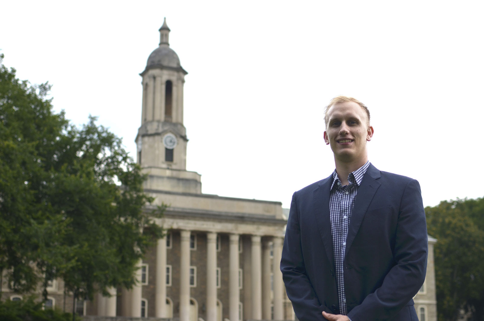 Scott Graupensperger is pictured wearing a suit jacket and collared shirt, standing in front of Penn State's Old Main building in State College, PA.