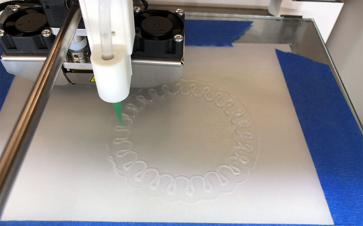 A 3D printing machine is seen, having printed a design of curlicues in silicone.