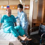A nurse helps a patient from a bed to a wheel chair.