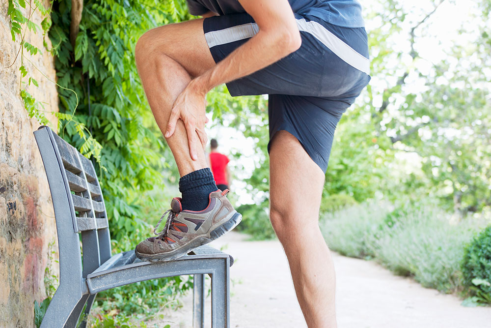 A male runner stretches left calf muscle on a bench in a stock photo.