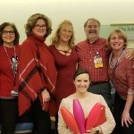 Members of the Pediatric Oncology team at Penn State Health Children's Hospital stand in a semi-circle. One woman kneels, holding in her arms a collection of bowling pins. The team is participating in in National Wear Red Day.