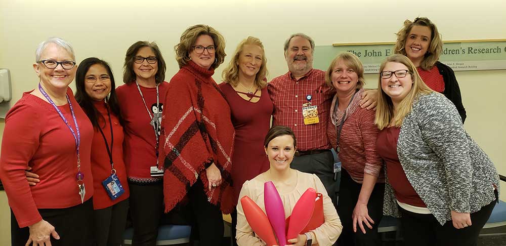 Members of the Pediatric Oncology team at Penn State Health Children's Hospital stand in a semi-circle. One woman kneels, holding in her arms a collection of bowling pins. The team is participating in in National Wear Red Day.