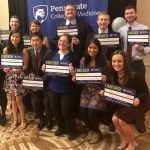 A group of Penn State College of Medicine students is pictured in front of a banner with the College logo on it. The students are each holding a sign showing the institution and speciality in which they will be completing residency.