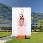 A portrait of a young boy holding a CMN trophy above his head, superimposed over an image of Penn State Health Children's Hospital.