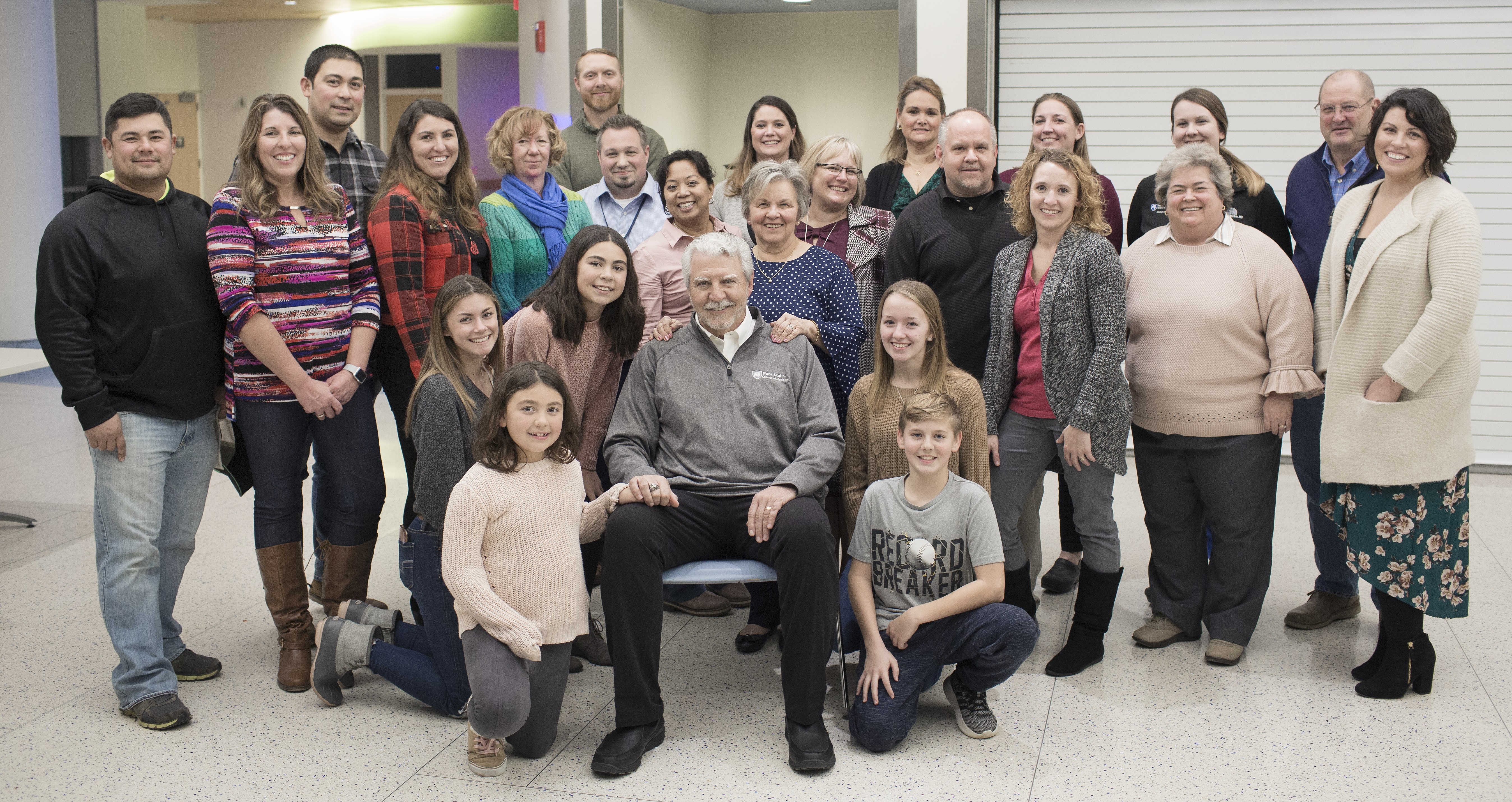Ed Frederick and his family pose for a photo with the staff at Penn State Health Milton S. Hershey Medical Center during the first “See Me Now” program. He is wearing a gray sweatshirt, collared shirt and slacks. Ed has white hair and a moustache and is seated in a chair in the middle of a group of 23 men, women and children.