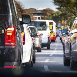 A line of cars are halted on a roadway. Their brake lights are illuminated.
