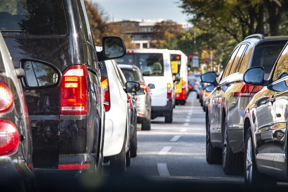 A line of cars are halted on a roadway. Their brake lights are illuminated.