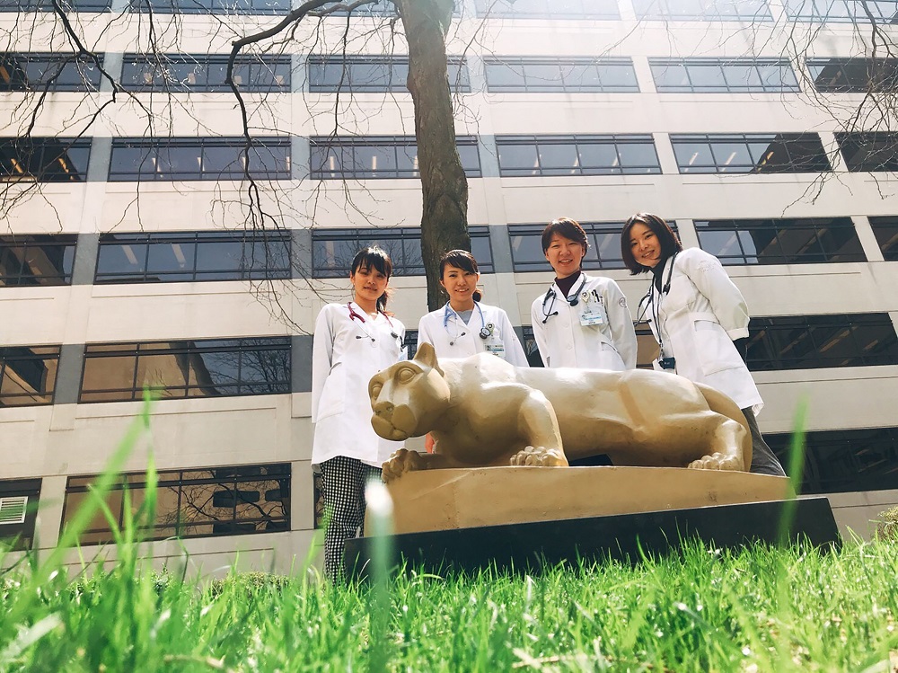 Four senior medical students from Tokyo Women’s Medical University stand behind the Penn State Nittany Lion in front of Penn State College of Medicine.