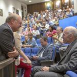 Dr. Craig Hillemeier talks with Dr. Carl June in a crowded auditorium.
